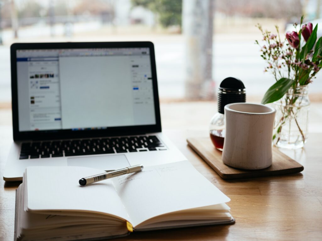 Laptop in the background with opened notebook and pen