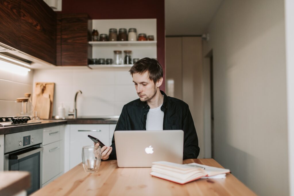 Man looking at smartphone laptop screen open, in kitchen