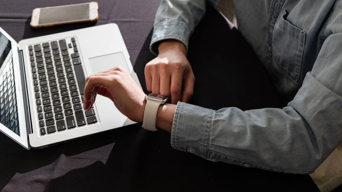 Person behind laptop, looking at their watch