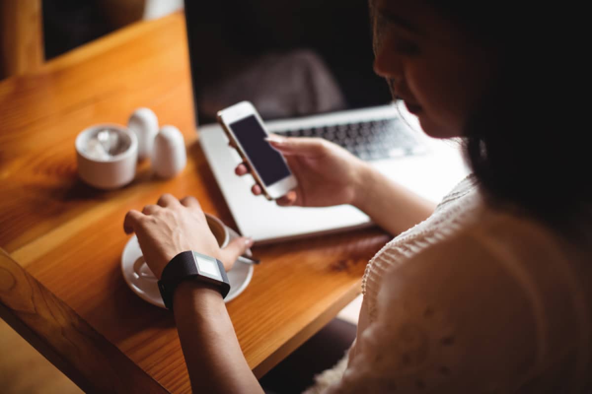 Woman checking the clock while holding phone and working on laptop