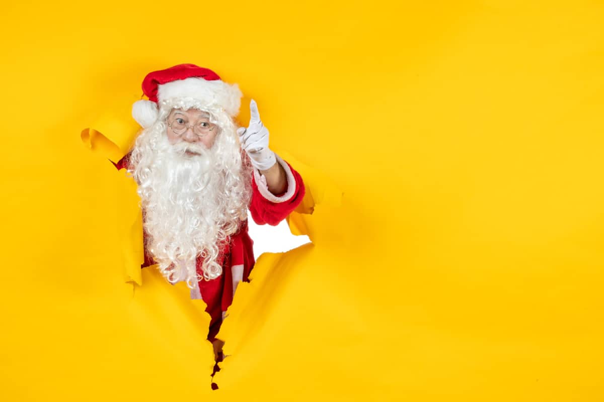 Santa looking through a yellow wall giving a warning sign