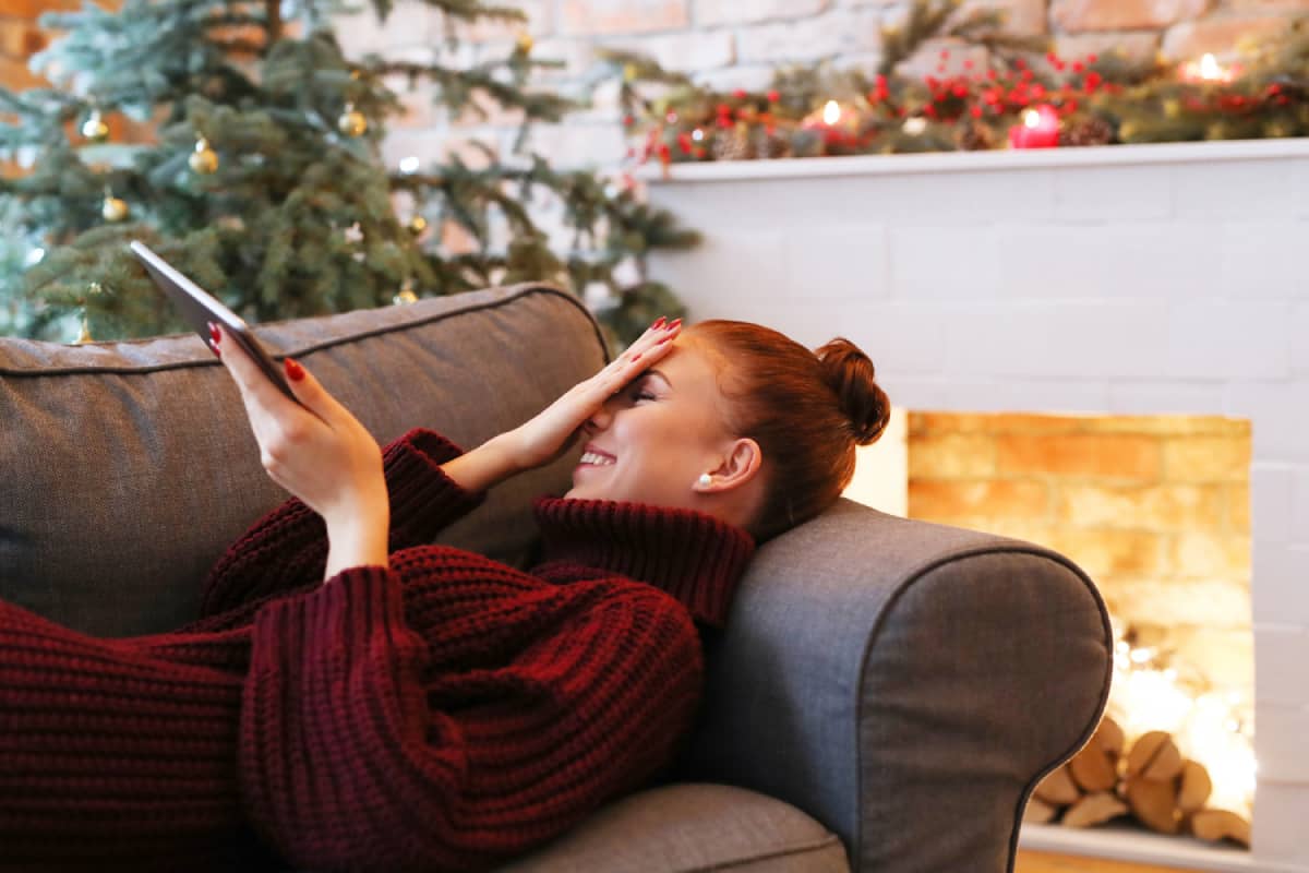 Woman at Christmas on a sofa holding a tablet phone and laughing