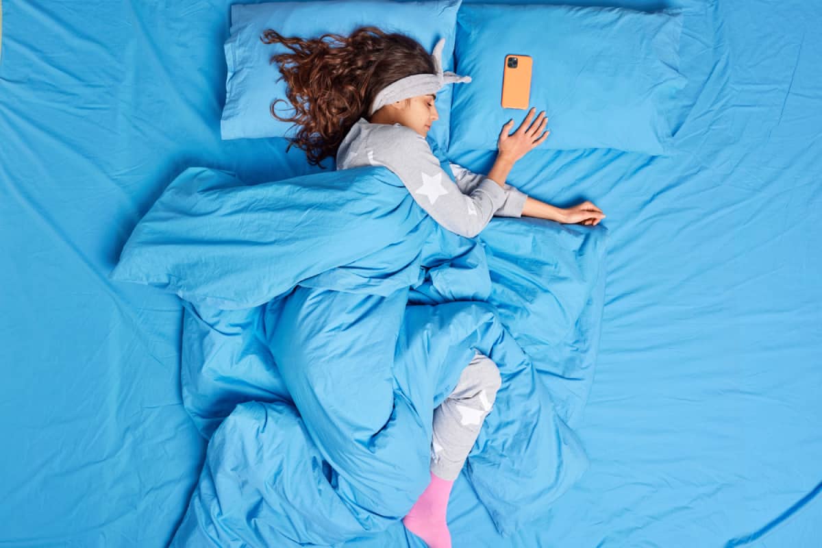 Woman sleeping in a blue bed next to her mobile phone