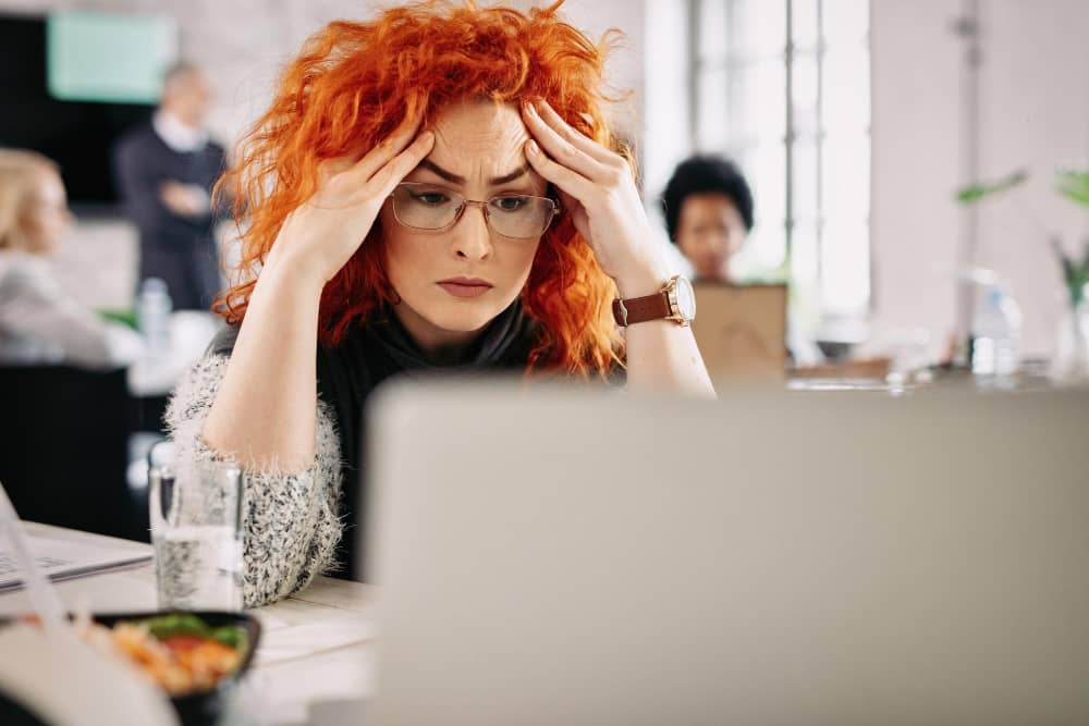 Exhausted tired woman working using laptop holding head hand, sitting at the office