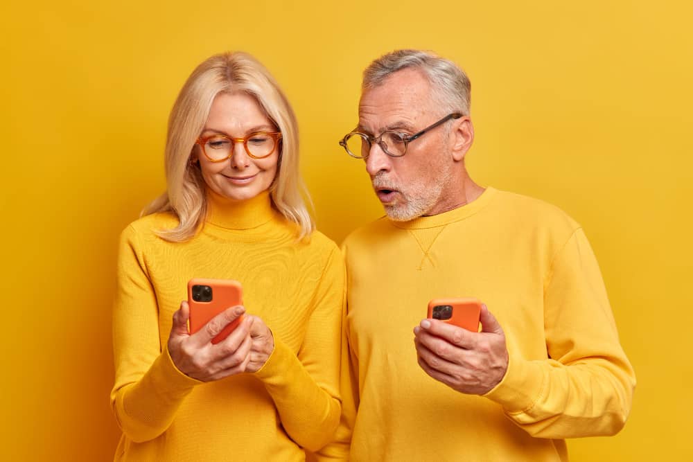 Older couple looking at their smartphones infront of isolated yellow wall