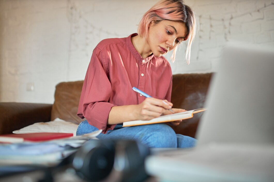 Woman with pink hair making notes behind laptop