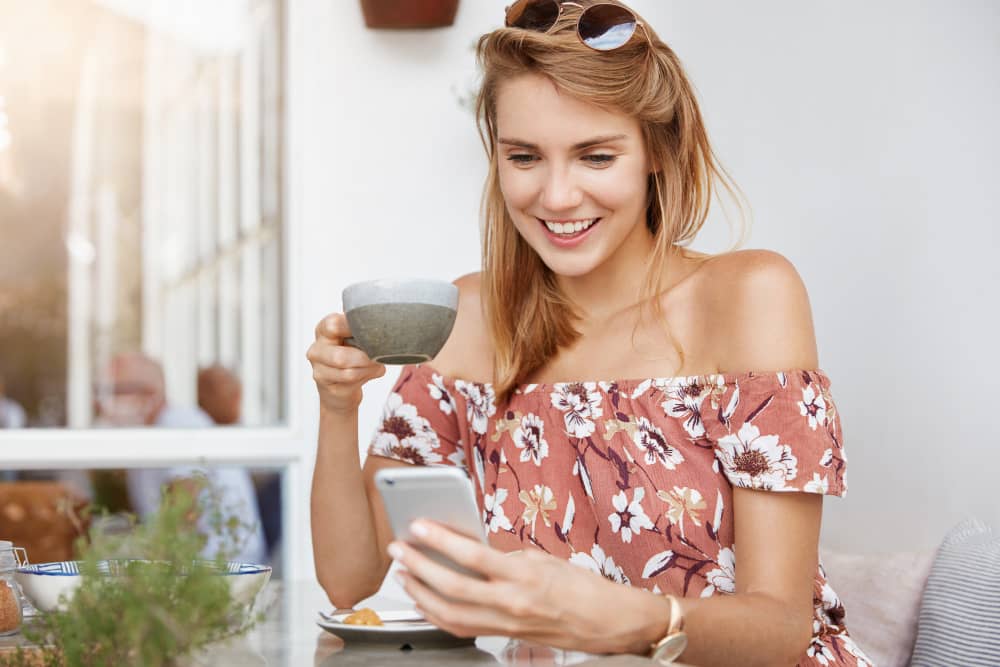 Young woman in a cafe reading a birthday email on her mobile phone