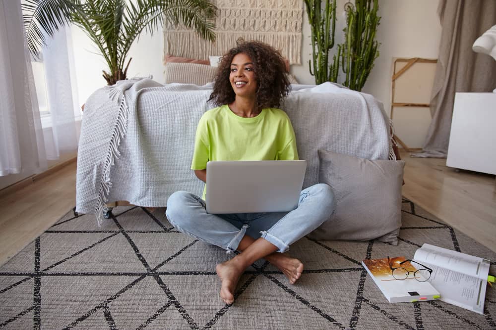 Cheerful young email marketer sitting on the floor with laptop