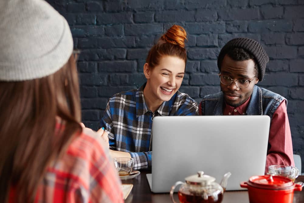 Team of young email marketers doing teamwork, discussing in front of laptop