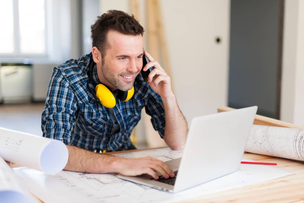 Smiling construction worker behind laptop doing email marketing