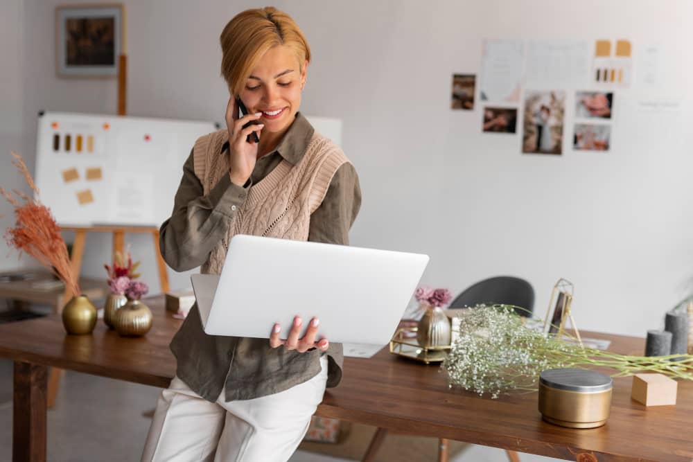 Happy working woman looking at her laptop, speaking on the phone