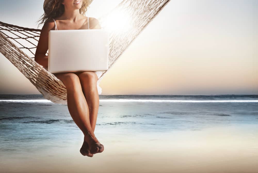 Woman with laptop sitting in a hammock at the beach as a tourist