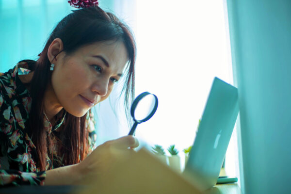 A woman looking at a computer with a magnifying glass, symbolizing the importance of accessible emails