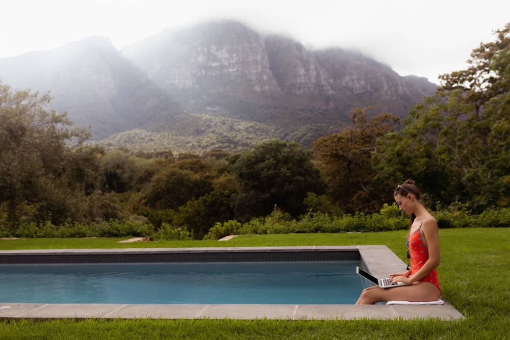 A woman on a laptop by the poolside in a tropical climate