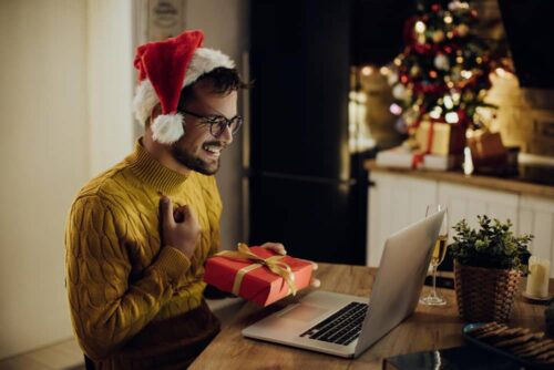 A man with a Christmas hat behind a computer, with a present in his hand