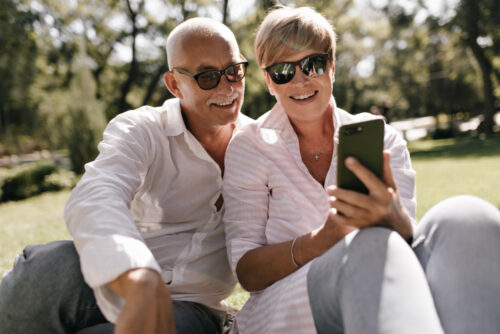 A Gen X couple sitting in the park, looking at a phone, laughing