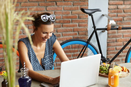 A woman laughing behind her laptop after engaging with funny content