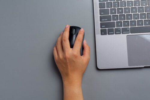 A person clicking a computer mouse on a gray table
