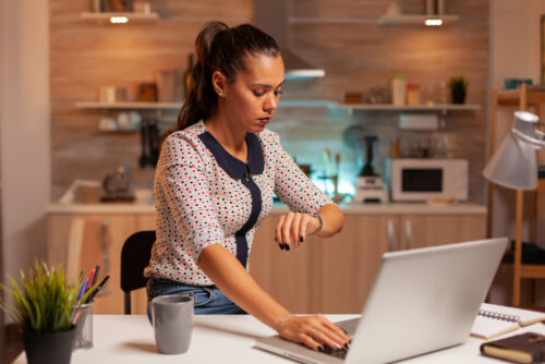 A woman checking the time while working on a laptop at home