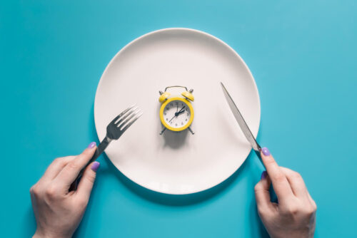 Person holding a knife and fork with a small clock on their plate, symbolizing everything time consuming