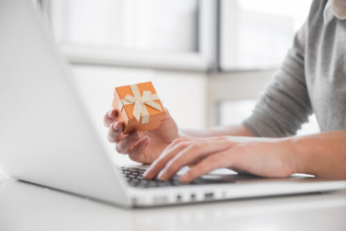 A person holding a gift in hand behind computer, symbolizing email marketing promotions