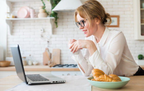 Happy, smiling woman drinking a cup of coffee and looking at her computer